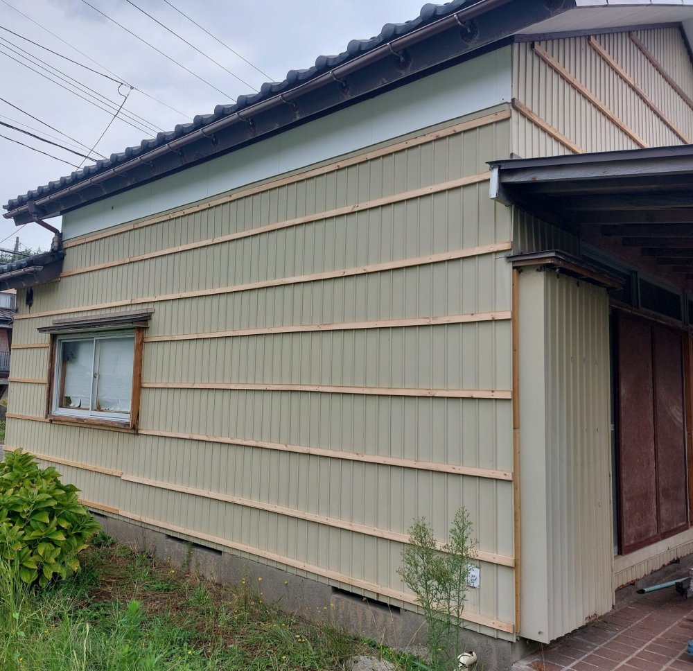 施工後の外壁。アイボリー系の金属外壁材に木材の桟を等間隔に配した住宅の側面